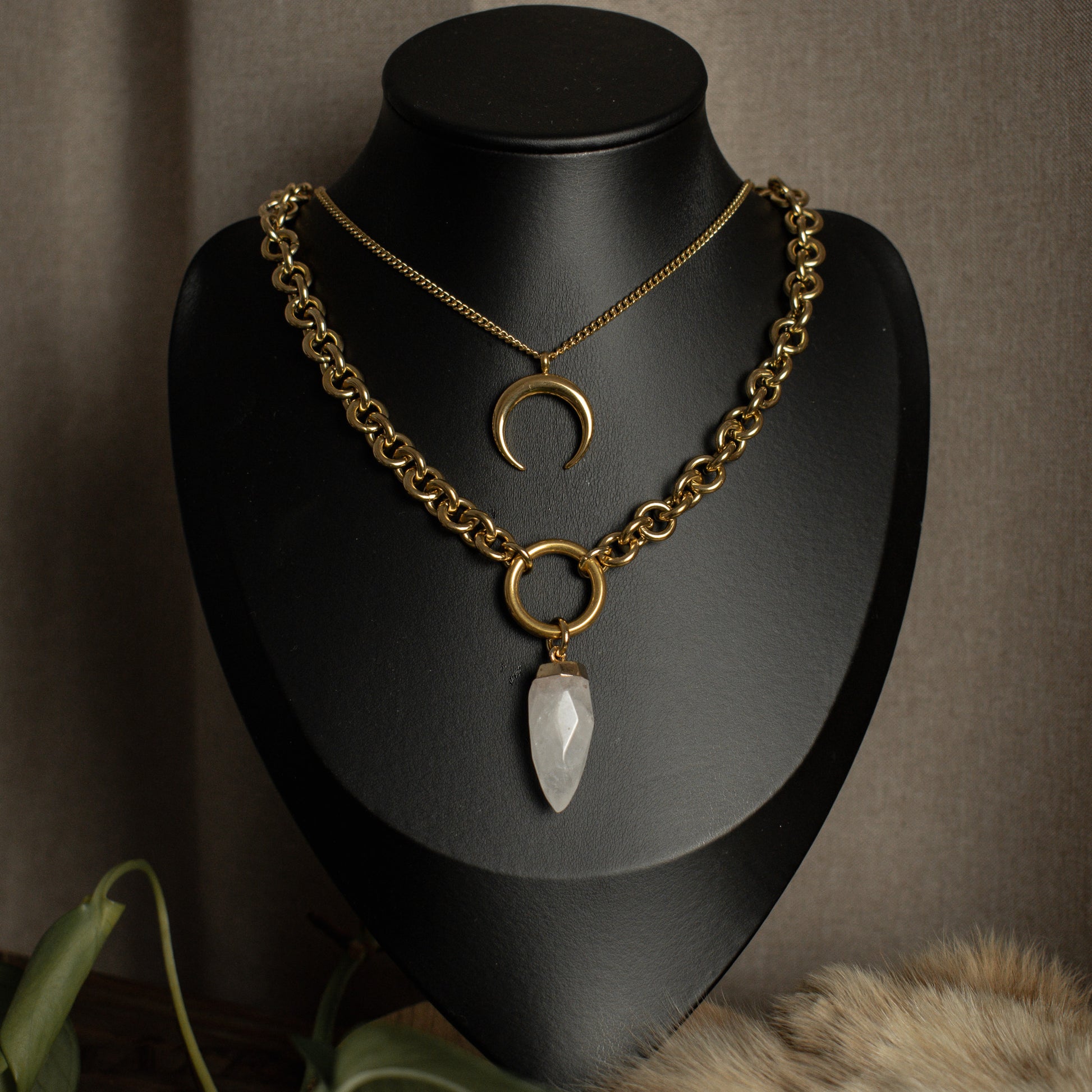 Gold chain necklace with crystal pendant on a black mannequin bust against a brown background