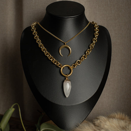 Gold chain necklace with crystal pendant on a black mannequin bust against a brown background