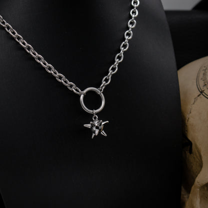 A silver medieval flail necklace with a chunky chain and a circular pendant, displayed on a black stand with a skull in the background.